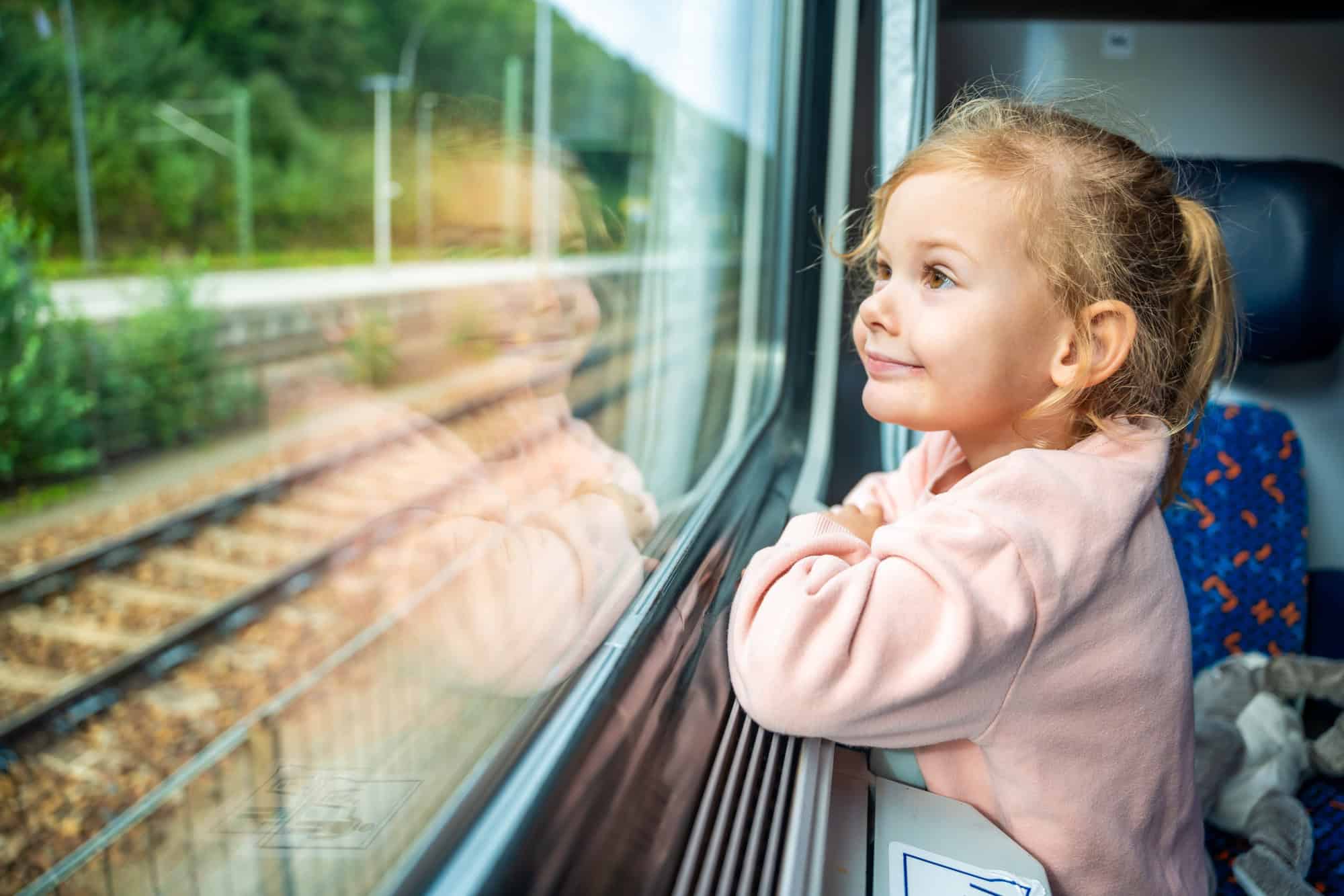 Happy little girl looking out train window outside, while it moving. Traveling by railway in Europe
