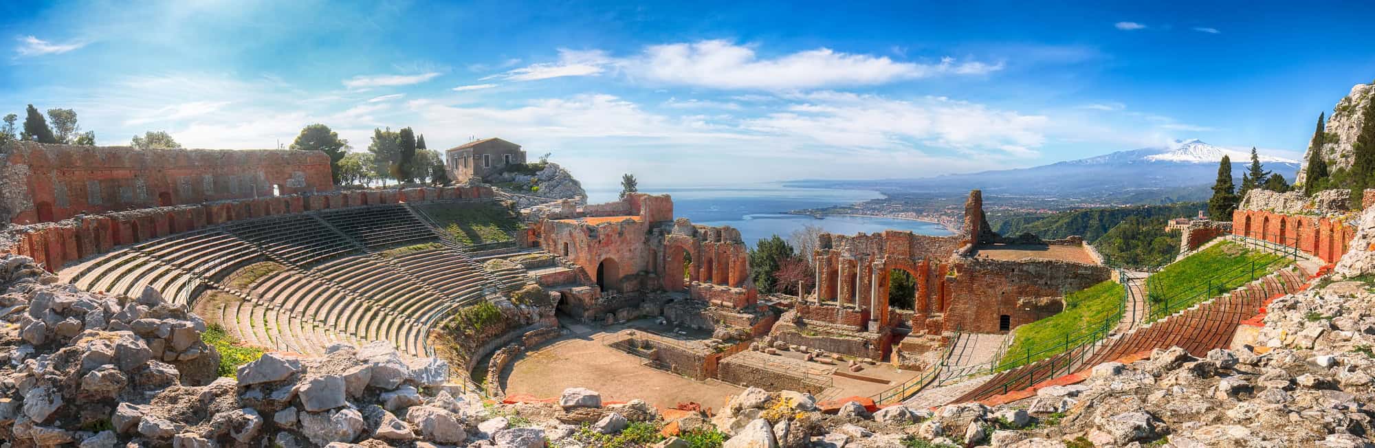 Ruins of ancient Greek theater in Taormina and Etna volcano in the background.