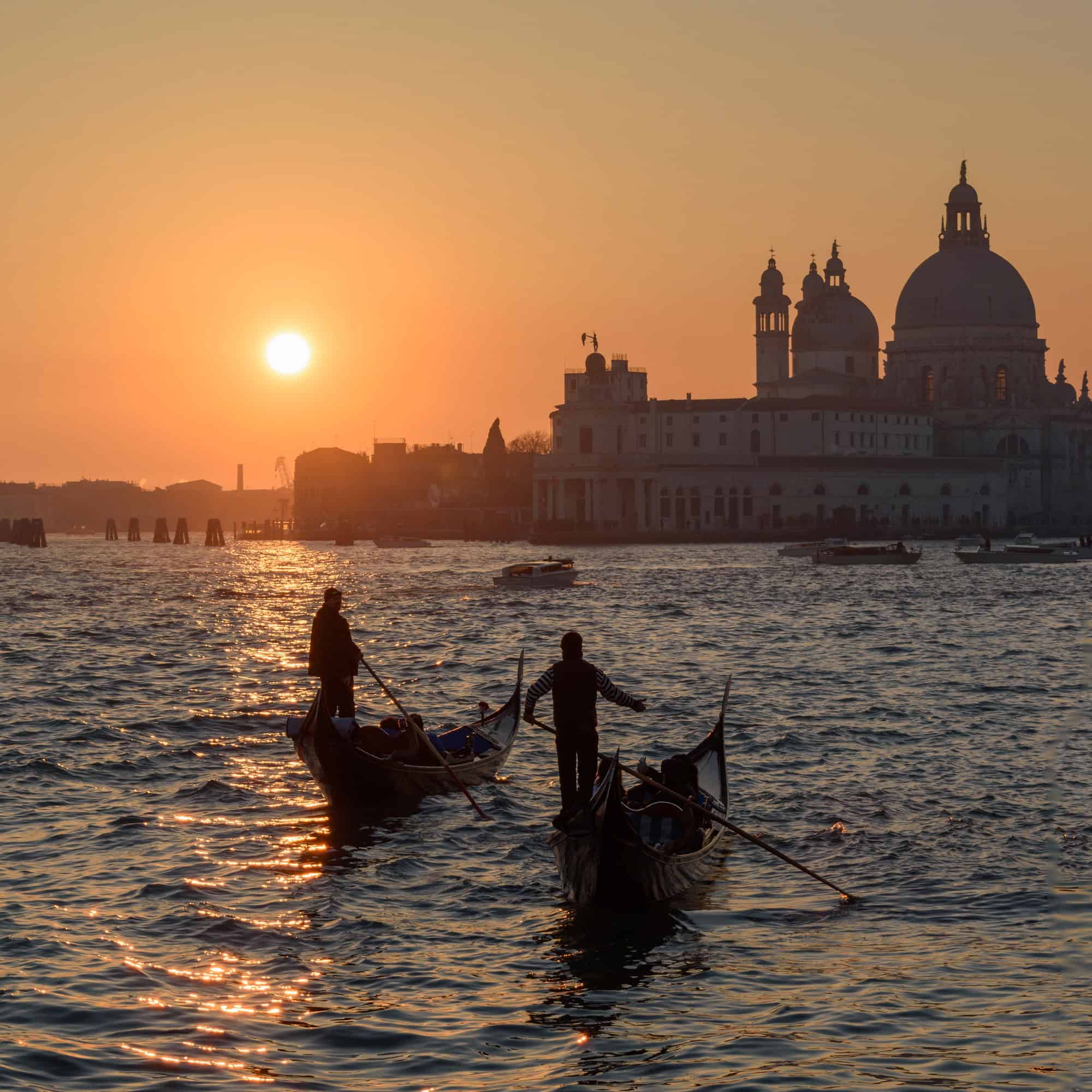 Two gondoliers on the Canale Grande in Venice, Italy, at sunrise, with the dome of Santa Maria della